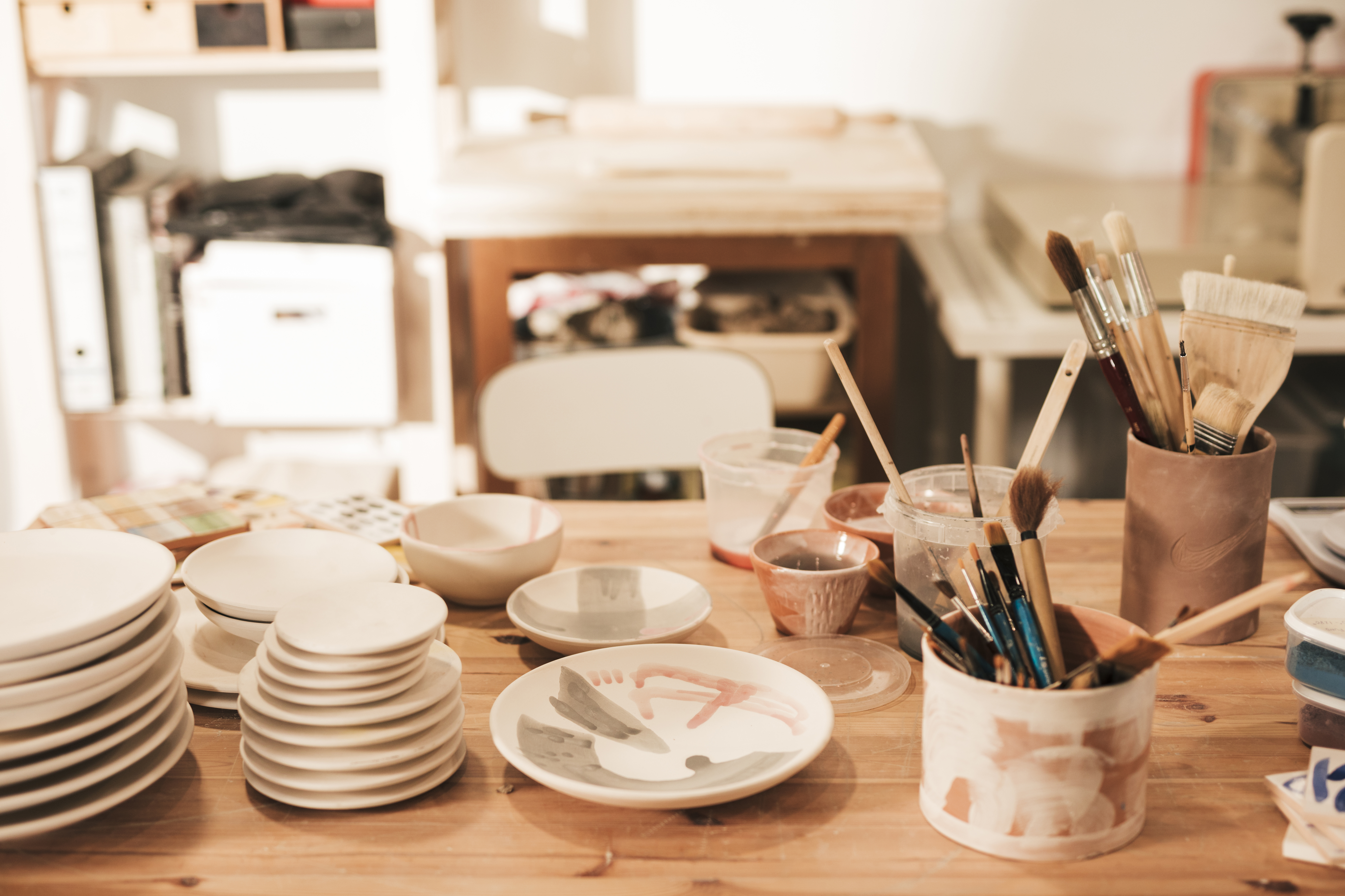 ceramic-plate-and-bowl-with-paint-brushes-and-tools-on-wooden-table-in-workshop
